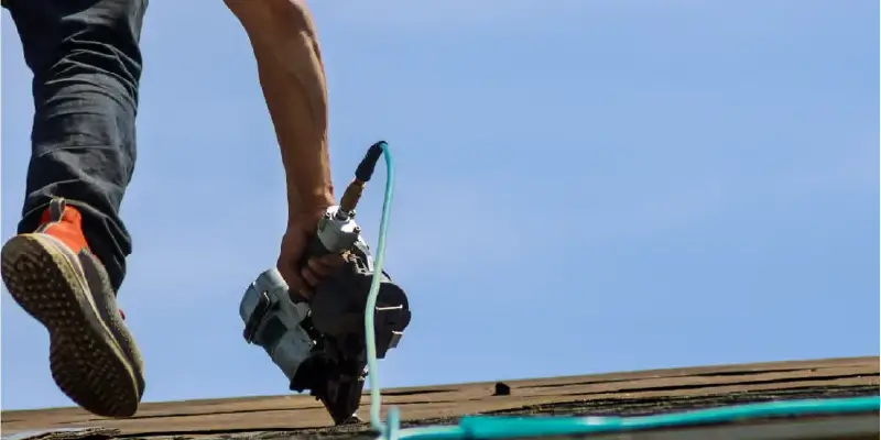 Image of a roofer using a nail gun to install shingles