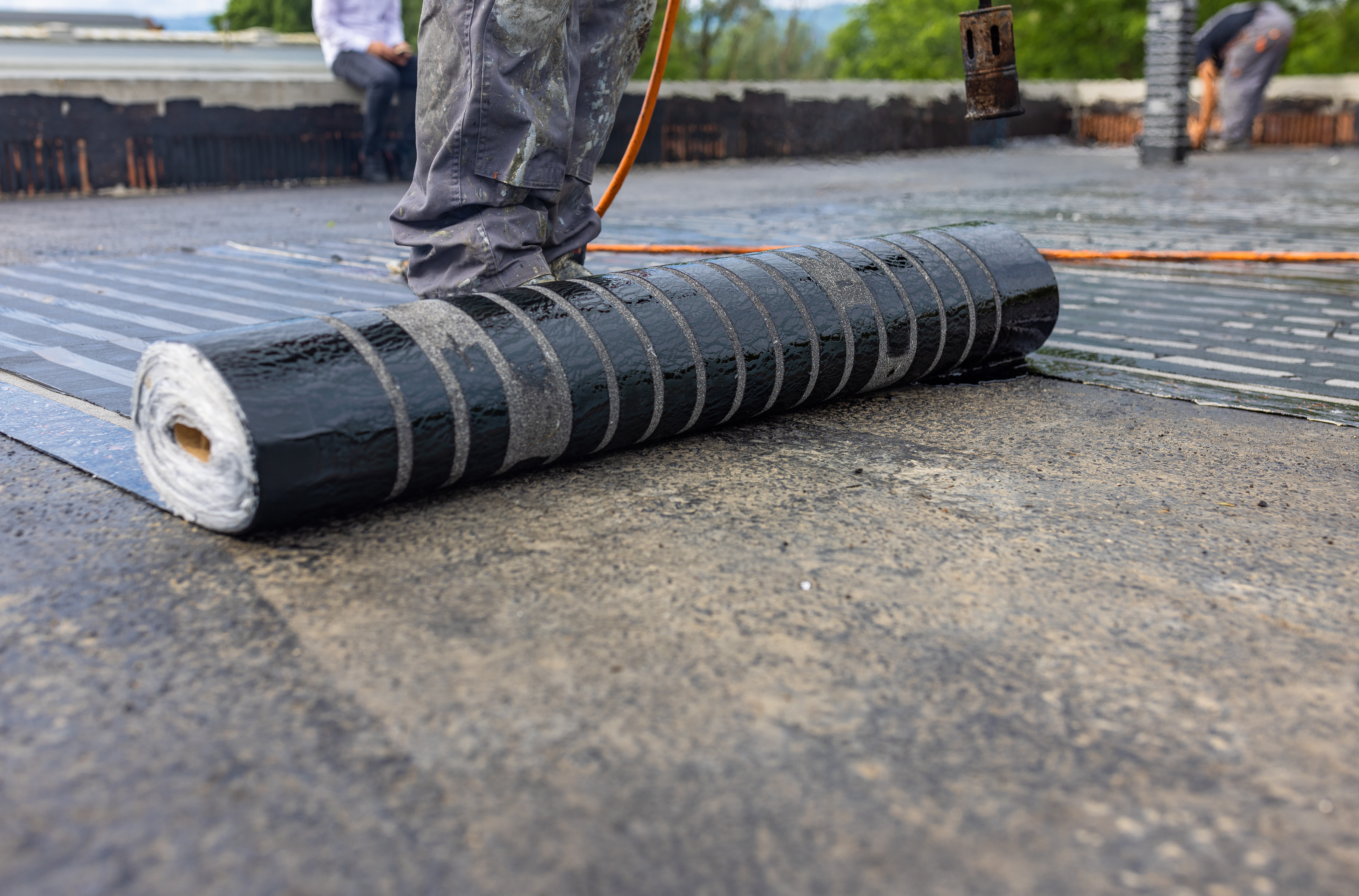 Image of a modified bitumen roofing being rolled out on a commercial building