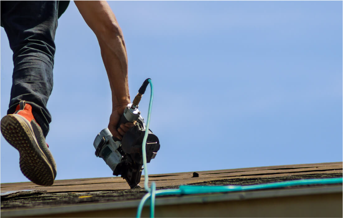 Image of a roofer using a nail gun to install shingles