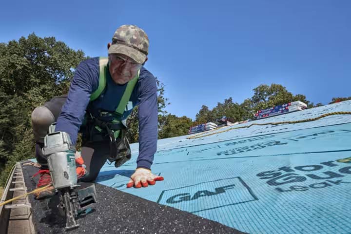 Image of a roof installer nailing starter shingles in place on a roof